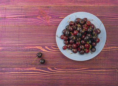 蓝板新鲜的烂熟樱桃在老木背景下设计蒙太奇。紫色木桌板纹理与磅甜樱桃顶部视图与复制空间