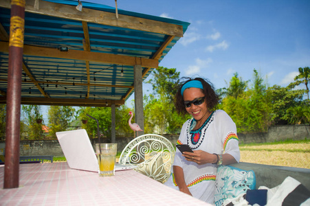 生活户外的年轻快乐和有吸引力的美国黑人混合族裔妇女与笔记本电脑和手机从美丽的咖啡馆在数字游牧人的工作概念工作的照片
