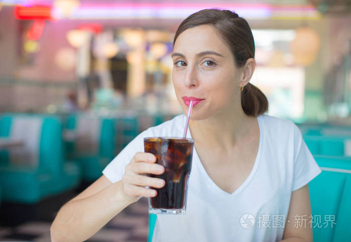 年轻漂亮的女人高兴和满意在美国餐厅喝可乐