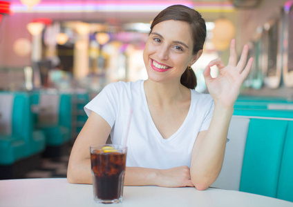 年轻漂亮的女人高兴和满意在美国餐厅喝可乐