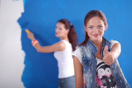 两个年轻漂亮的女人手持调色板, 站在墙边。两个年轻漂亮的女人
