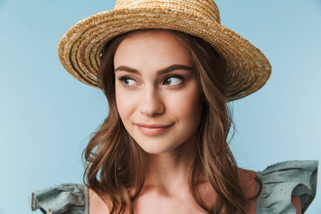 关闭一个微笑的女人在礼服和夏天的帽子看着远离蓝色背景孤立的肖像