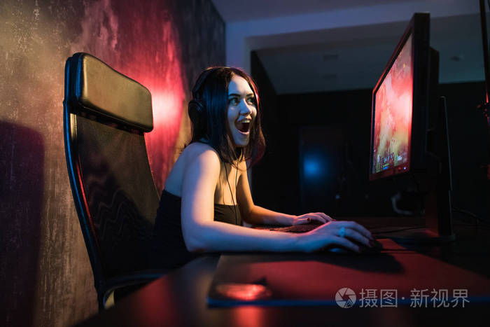 一个可爱的女玩家女孩坐在一个舒适的房间在电脑后面玩游戏.