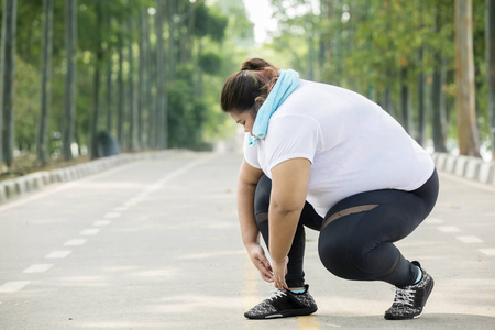 穿着运动服的胖女人的照片和她的鞋带绑在路上
