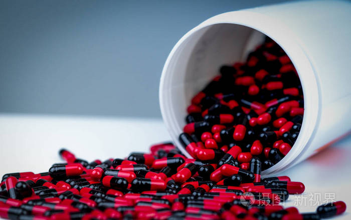 红黑抗生素胶囊丸从白色塑料瓶容器中溢出.制药行业.处方药.四环素药.