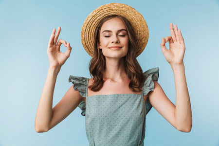 关闭在礼服和夏天的帽子平静的女人的肖像显示确定的手势孤立的蓝色背景