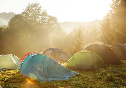 日出时在绿色草地上的旅游帐篷。露营背景