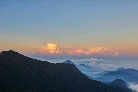 群山之间山谷之间的山与雾和卷曲的云彩照亮了上升的太阳
