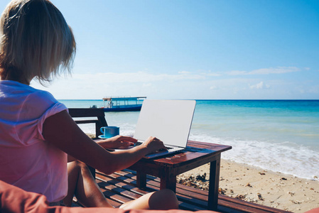 年轻的千年女孩键盘发表博客在上网本上使用良好的无线互联网连接在海洋海滩上, 商务妇女享受自由职业者的工作使用笔记本电脑近海
