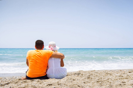 浪漫情侣在休闲服装坐在沙滩上, 并期待海
