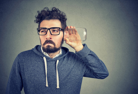 年轻滑稽的人偷听玻璃罐子看可疑, 而听秘密, 私人谈话照片