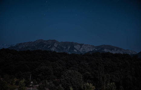 美丽的夜晚景观与繁星夜山和森林。夜森林与绿色草甸和山在明亮的繁星夜或银河看法