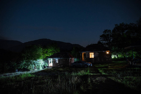 晚上在森林里建筑的山夜风景与月亮或老式乡下房子在晚上与云彩和星。夏日之夜。照片拍摄与长期曝光