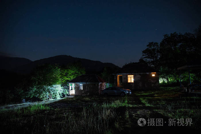 晚上在森林里建筑的山夜风景与月亮或老式乡下房子在晚上与云彩和星.