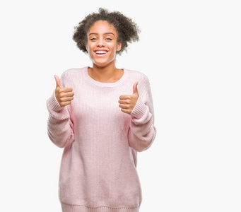 年轻的美国黑人妇女穿着冬季毛衣在孤立的背景下成功标志做积极的手势与手, 大拇指向上微笑和快乐。看着带着欢快表情的相机, 胜利者的