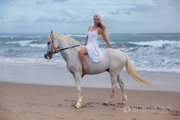 性感的年轻女子步行与马在沙滩上, 马背上
