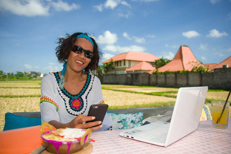 生活户外的年轻快乐和有吸引力的美国黑人混合族裔妇女与笔记本电脑和手机从美丽的咖啡馆在数字游牧人的工作概念工作的照片