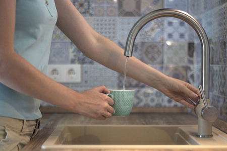 年轻女子从厨房水龙头里倒水.照片