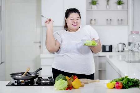 在厨房里吃健康沙拉时, 胖女人微笑着拍照的照片