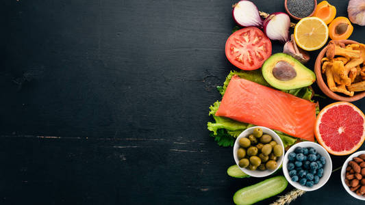 一套健康的食物。鱼, 坚果, 蛋白质, 浆果, 蔬菜和水果。在黑色的木质背景。顶部视图。文本的可用空间
