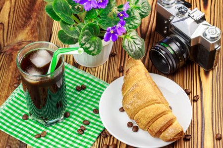 下了杯黑咖啡，冰和小管对绿色的餐巾。羊角面包，老式相机，花盆，木桌