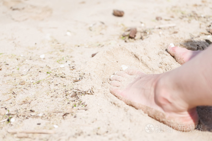 一个女人的脚与白色的钉子在海滩沙子在阳光下