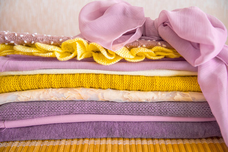 桌子上的一堆衣服。黄色紫色和粉红色。针织夹克丝巾