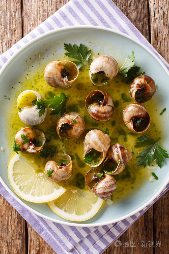 辛辣的法国蜗牛, 田螺用黄油,欧芹,柠檬和大蒜在桌子上的盘子上做的