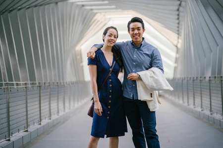 一个亚洲华人夫妇的肖像在周末的日期。这名男子年轻, 英俊, 衣着考究, 女士穿着优雅的夏日礼服。他们在桥上