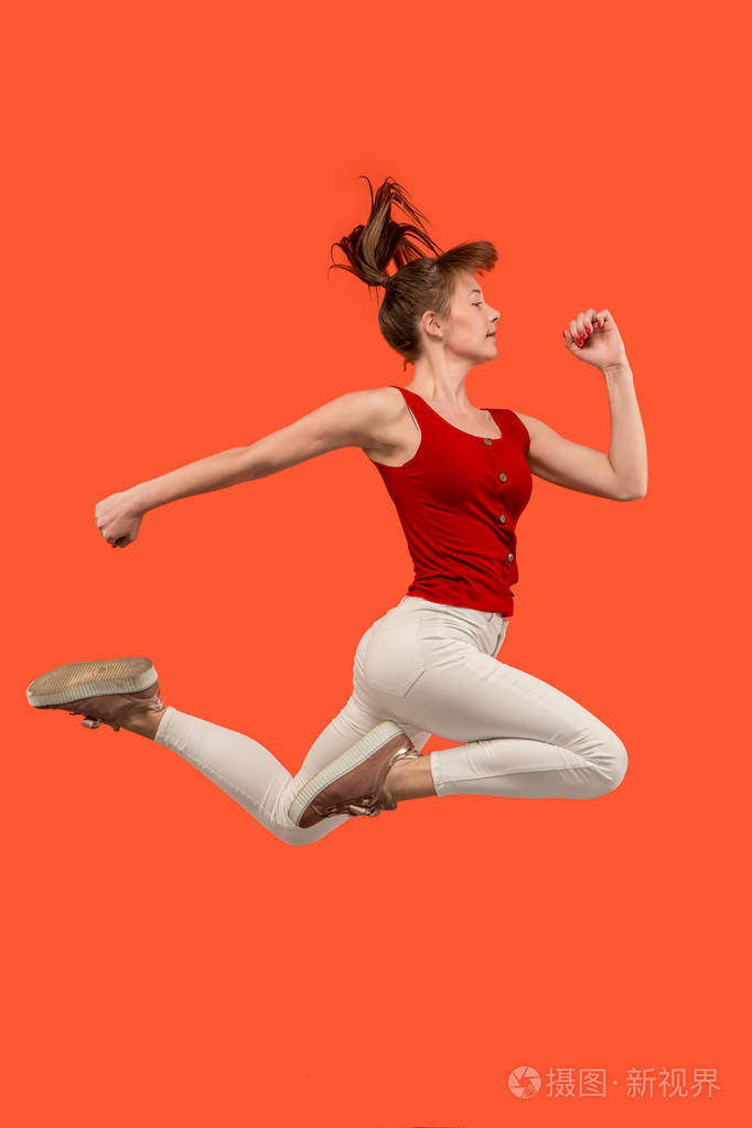 自由移动.漂亮的年轻女子跳反对橙色背景
