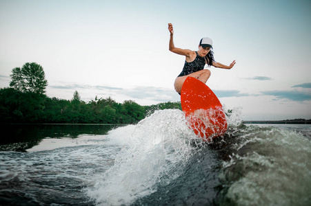 年轻迷人的黑发女子跳上橙色 wakesurf 在摩托艇的背景下的浪