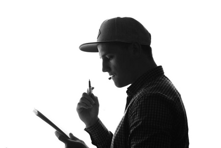 后面的一个年轻体贴的男子在帽子持有笔在鼠标和笔记本在手。剪影。黑白相间