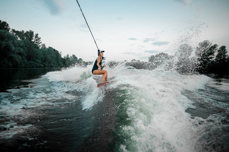 年轻迷人的黑发女孩骑在 wakesurf 拿着一根摩托艇的绳子在树的背景上