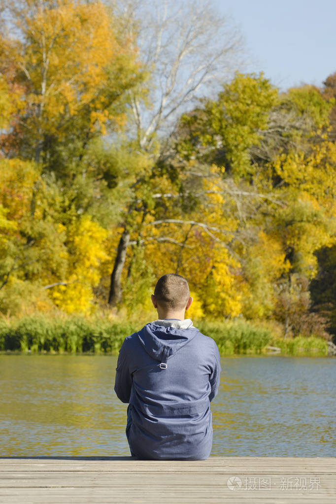 一个年轻人坐在码头上秋天晴朗的日子后退视图