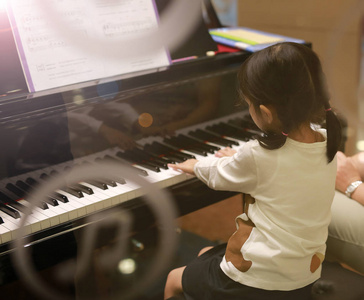 小女孩弹钢琴。从外部玻璃查看