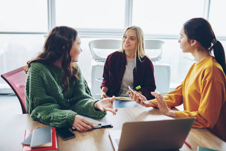 女性设计师的积极乘员组在 coworking 办公室的合作过程中进行了交谈, 年轻女子向她的同事解释了她坐在笔记本电脑旁边的规划