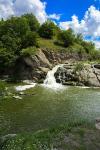 河上的瀑布流经和越过覆盖着苔藓和苔藓的岩石, 在绿色植被和蓝天的背景下