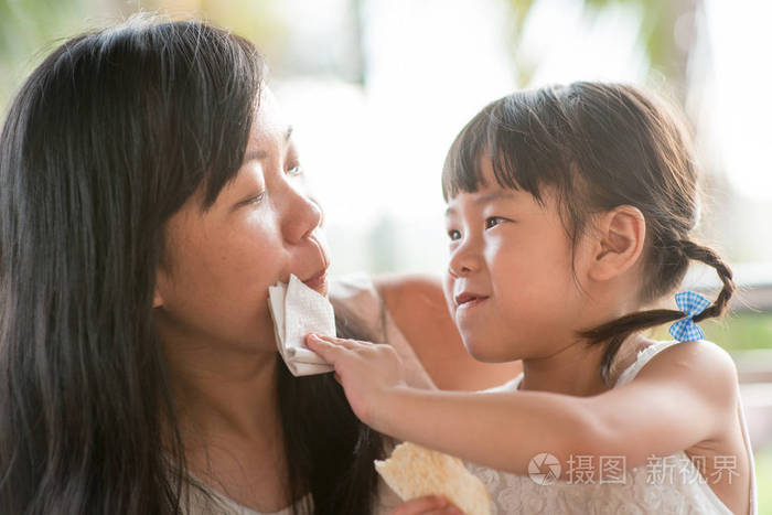 孩子在咖啡馆给妈妈擦嘴。亚洲家庭户外生活方式与自然光