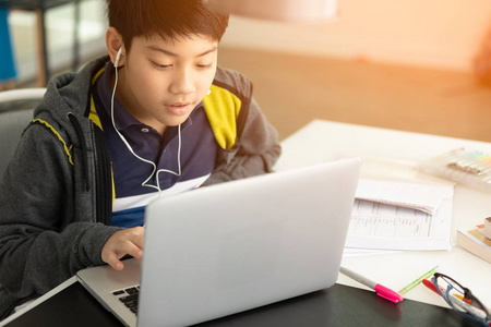 亚洲逗人喜爱的男孩使用笔记本电脑与阳光在早晨在家
