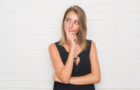 美丽的年轻妇女在白色砖墙严肃的面孔思考问题, 非常迷惑想法照片