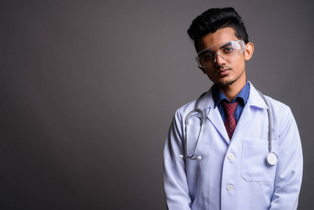 戴防护眼镜的年轻印度男子医生对灰色