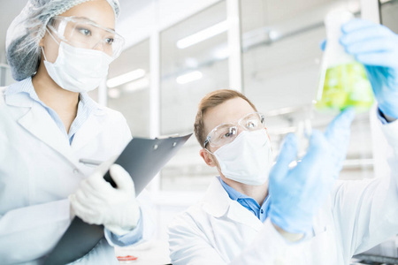 两位现代科学家的肖像在实验室里坐在桌子旁研究烧杯中的绿色液体