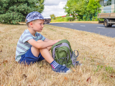 日视图小男孩旅行者与背包坐在英国路旁边