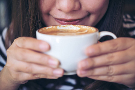 亚洲妇女闻和喝热咖啡的特写图片在白色杯子与感觉好在咖啡馆