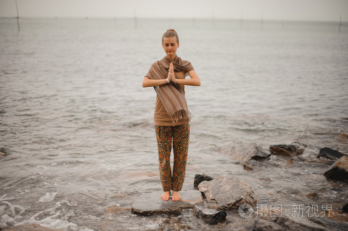 女人站感激合十瑜伽构成在海滩旁边的海洋中多云的天气.禅,冥想,和平