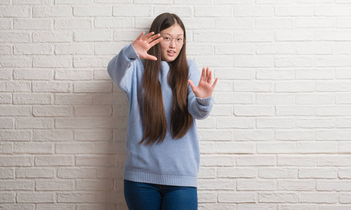 年轻的中国女人在白砖墙上害怕和惊恐的表情, 用手停止手势, 在休克中大叫。恐慌概念