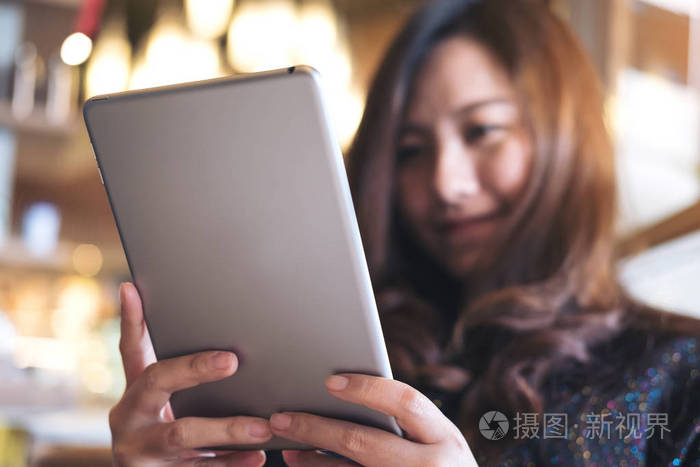 一个美丽的亚洲女人, 带着笑脸在现代咖啡馆里手持和使用平板电脑