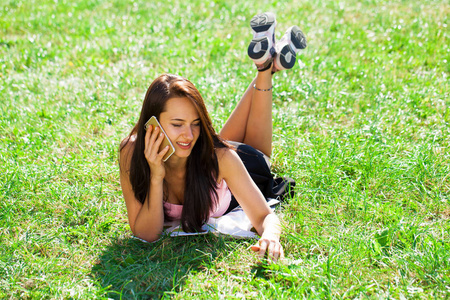 快乐美丽的黑发女孩电话在夏日公园打电话