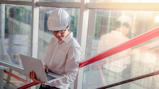 年轻的亚洲男性工程师或建筑师, 在施工现场佩戴防护安全帽时, 在