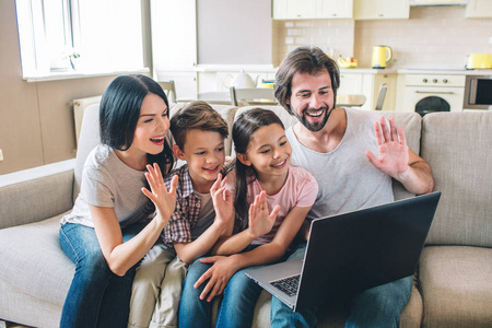 开朗的家庭有笔记本电脑和波浪与他们的手。他们在 skype 上交谈。漂亮的人在微笑